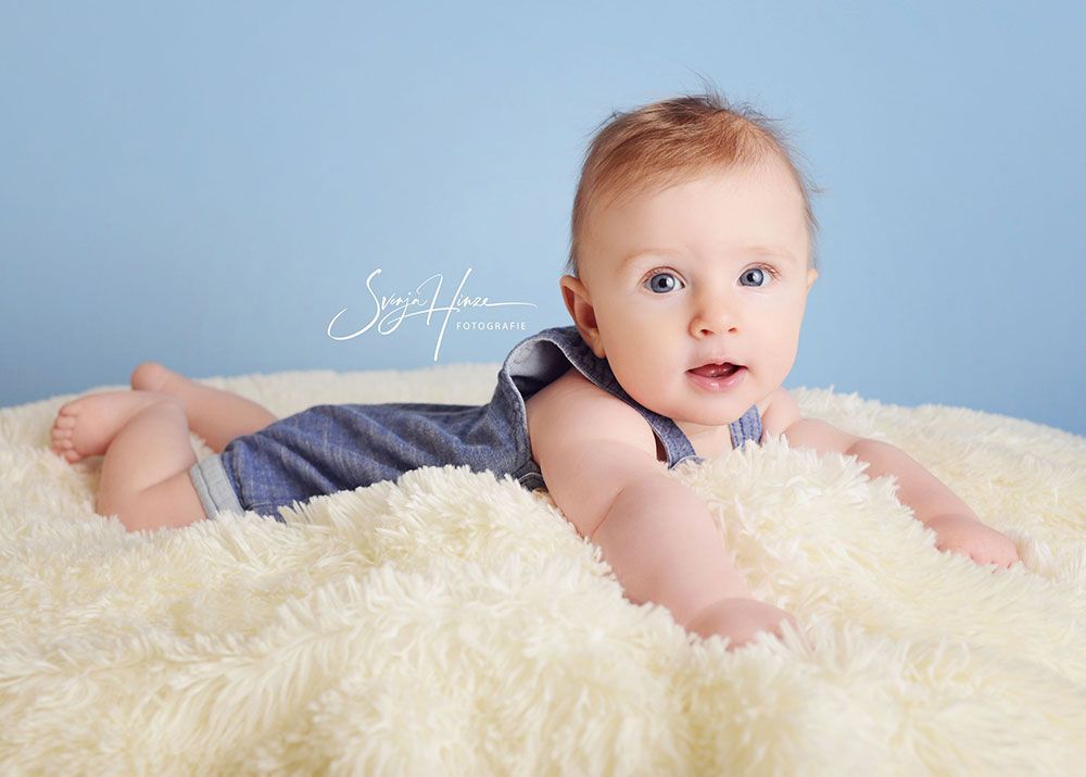 Ein Baby liegt auf einer weißen Decke und schaut in die Kamera.