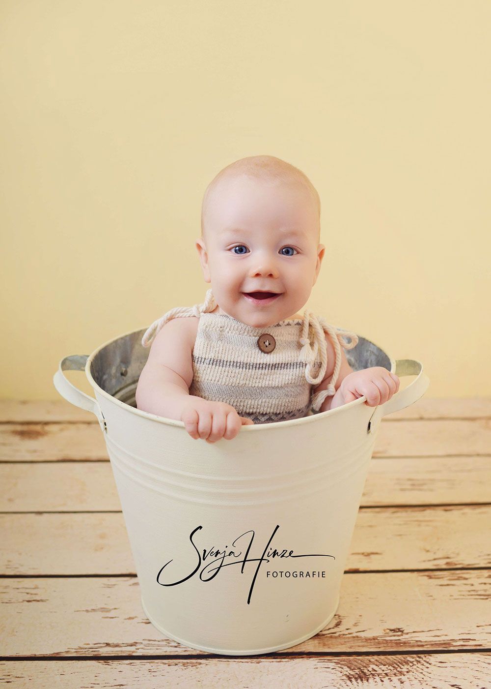 Ein Baby sitzt in einem weißen Eimer auf einem Holztisch.