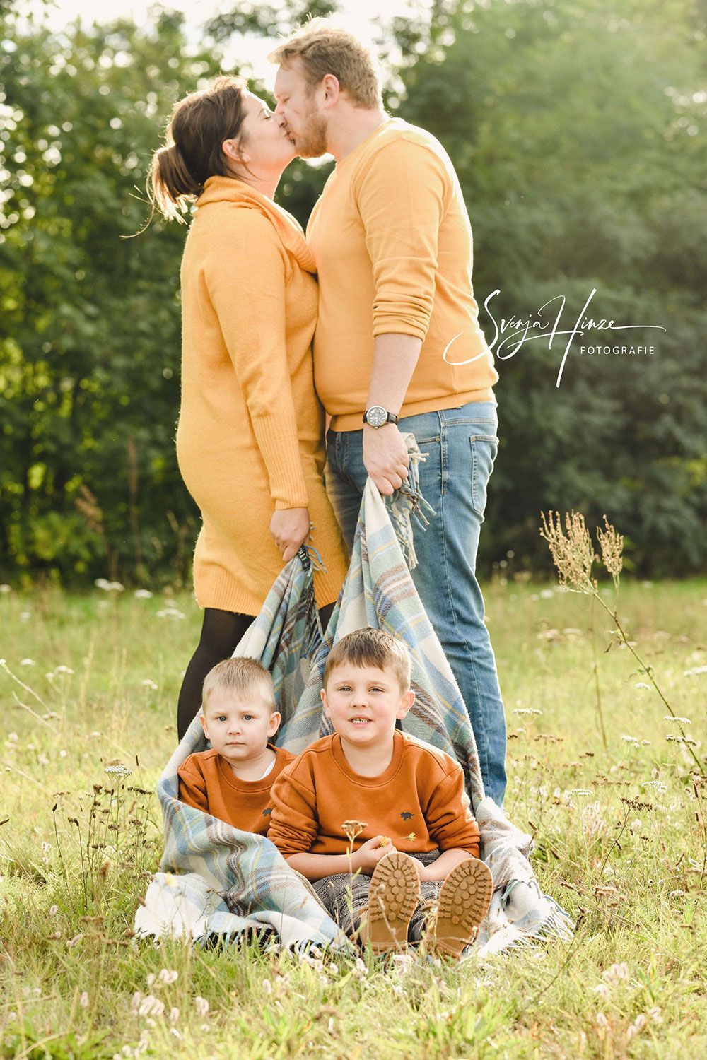 Ein Mann und eine Frau küssen sich, während zwei Jungen auf einer Decke auf einem Feld sitzen.