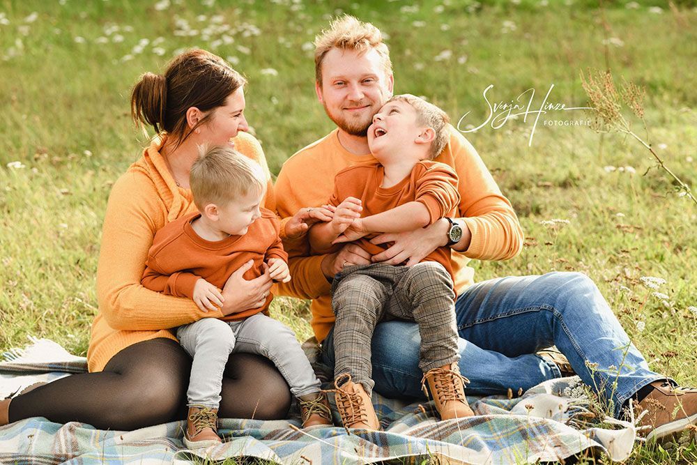 Eine Familie sitzt auf einer Decke im Gras.