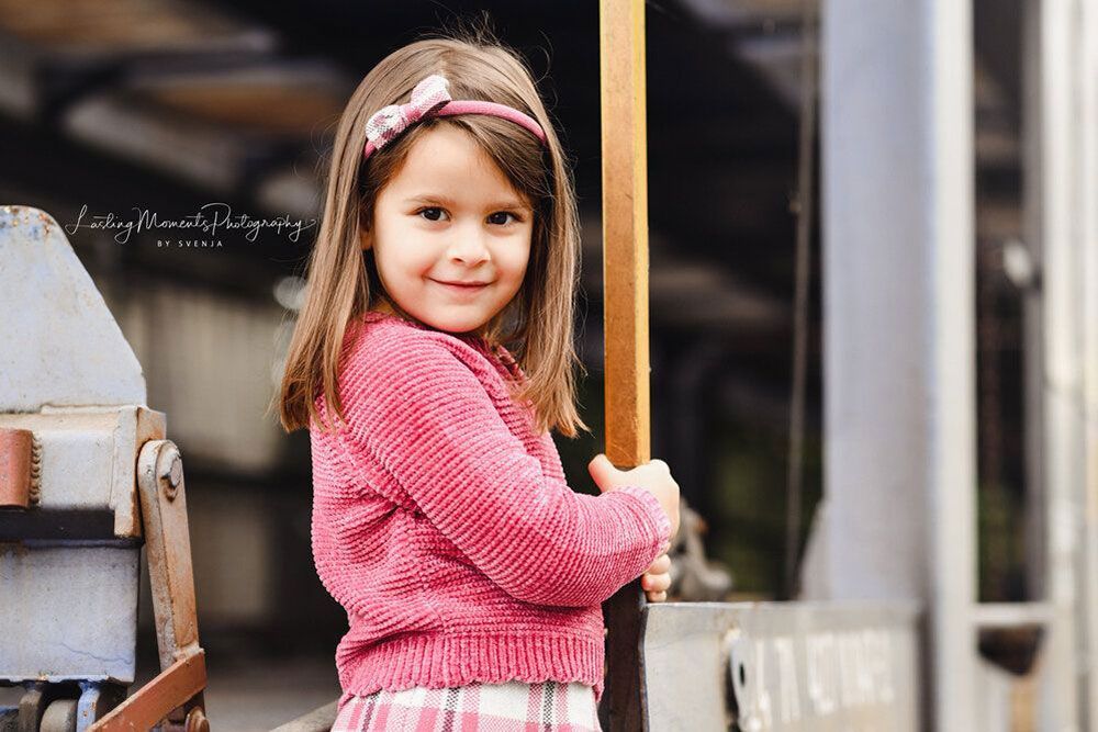 Ein kleines Mädchen in einem rosa Pullover und einem karierten Rock hält einen Holzstab.