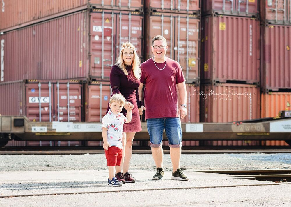 Eine Familie steht vor einem Stapel Frachtcontainer.