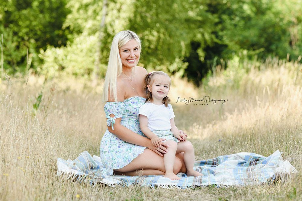Eine Frau und ein kleines Mädchen sitzen auf einer Decke auf einem Feld.