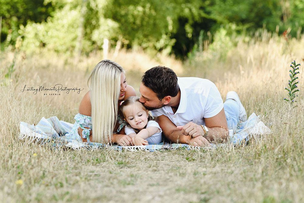 Eine Familie liegt auf einer Decke im Gras.