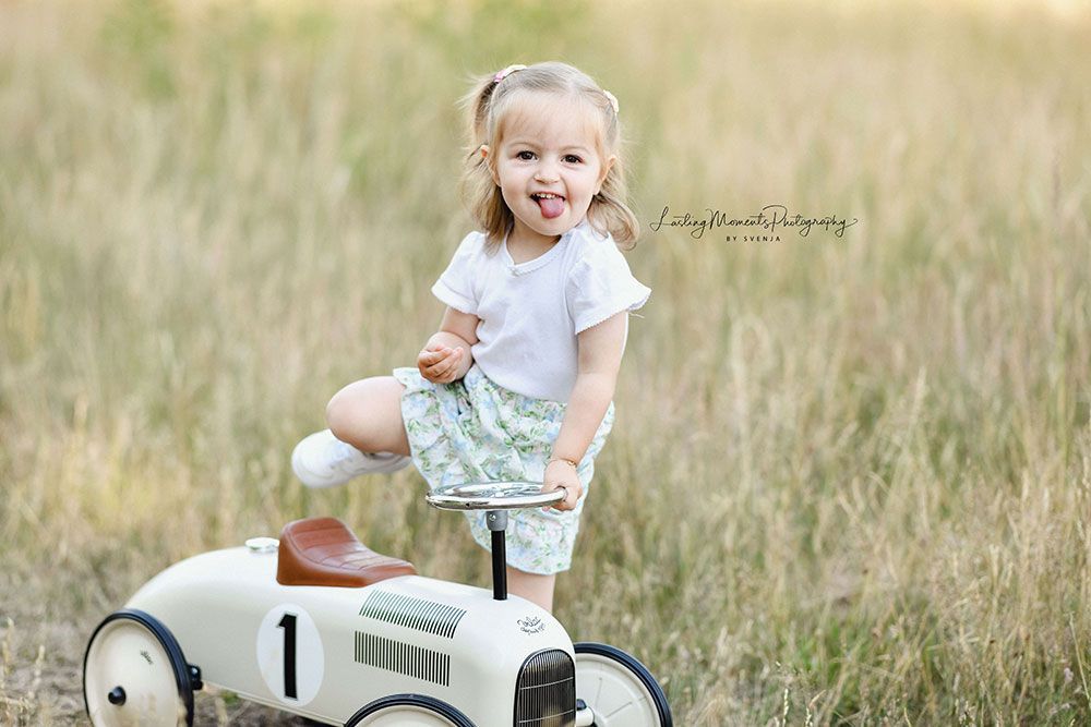 Ein kleines Mädchen sitzt auf einem Spielzeugauto auf einem Feld.