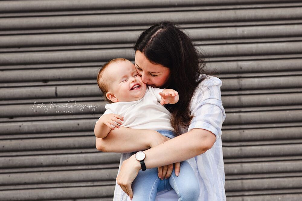 Eine Frau hält ein Baby in ihren Armen und küsst es auf die Wange.