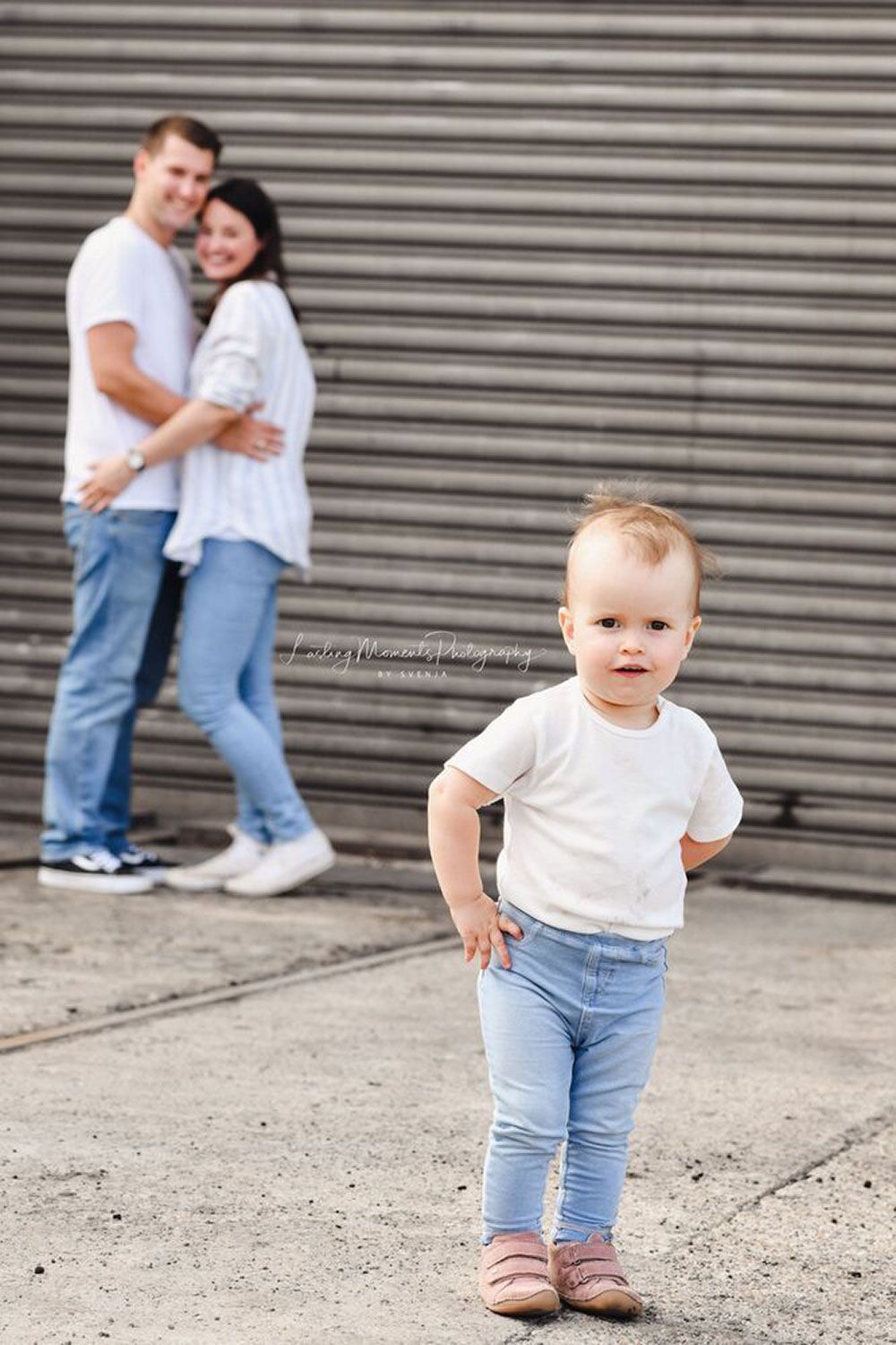 Ein Baby steht vor einem Mann und einer Frau.