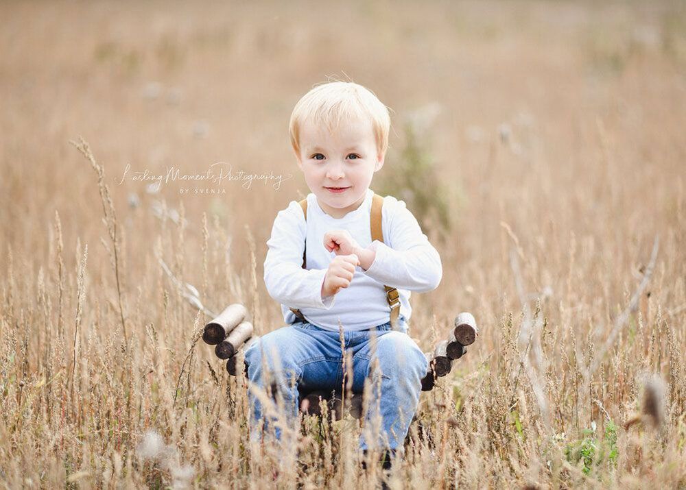 Ein kleiner Junge sitzt auf einem Hocker auf einem Feld.