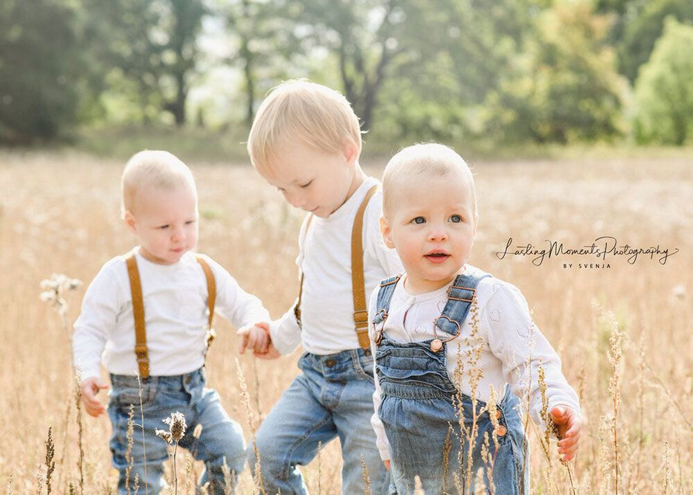 Drei kleine Jungen stehen mit Hosenträgern auf einem Feld.