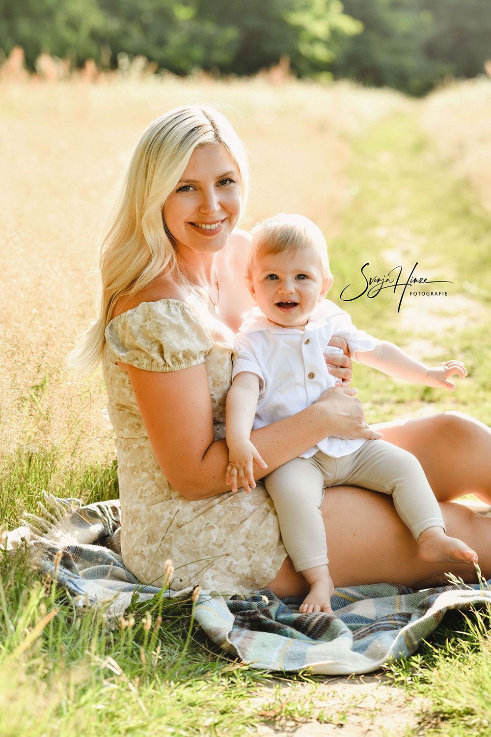 Eine Frau sitzt auf einer Decke auf einem Feld und hält ein Baby.