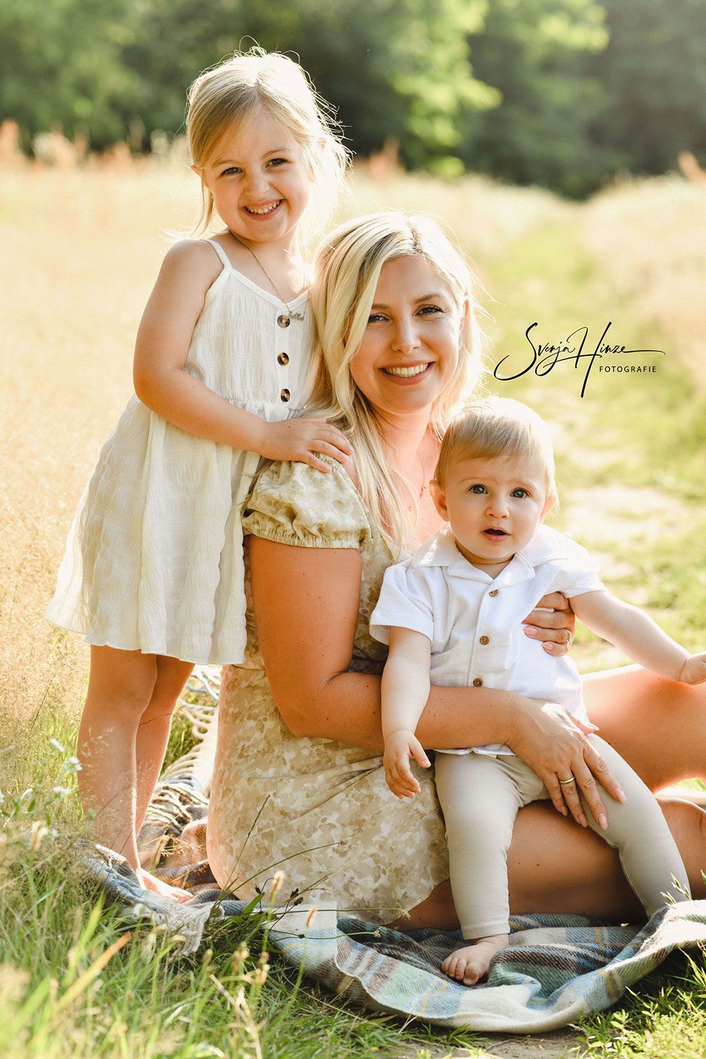 Eine Frau sitzt mit zwei Kindern im Gras.