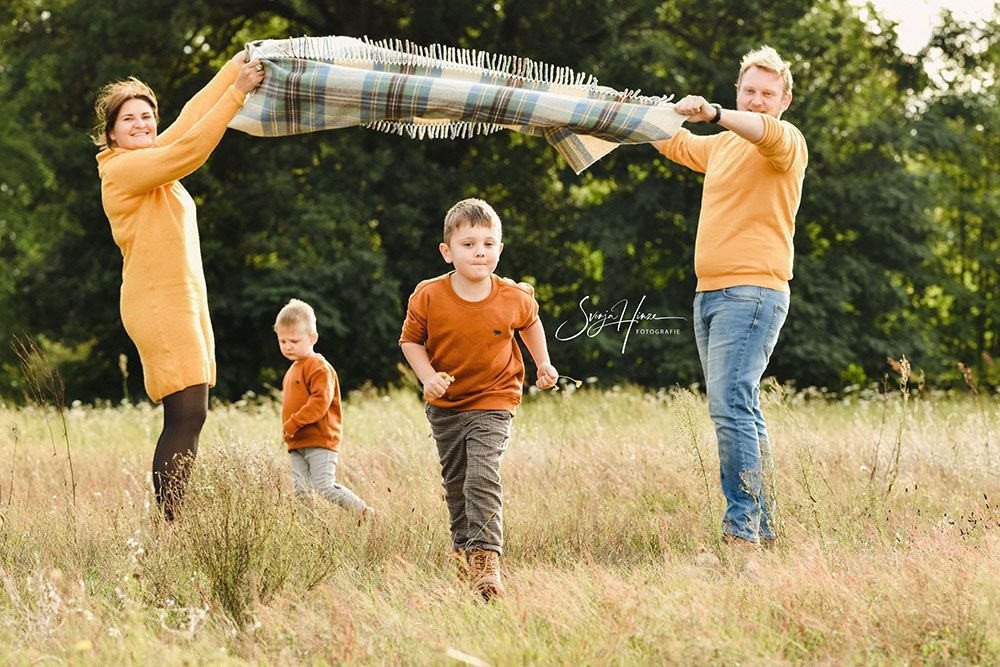 Eine Familie spielt mit einer Decke auf einem Feld.