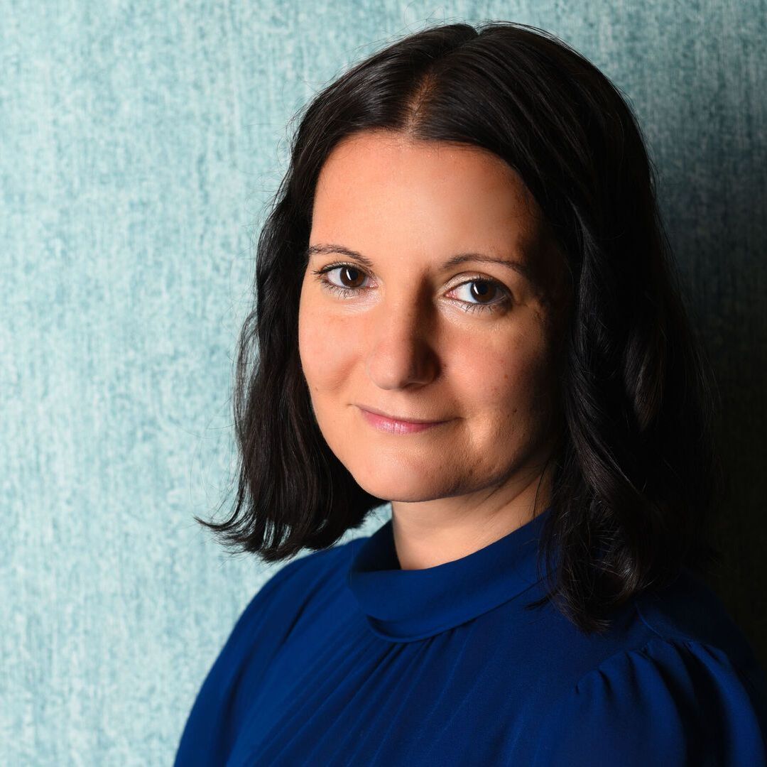Eine Frau in einem blauen Hemd steht vor einer blauen Wand.