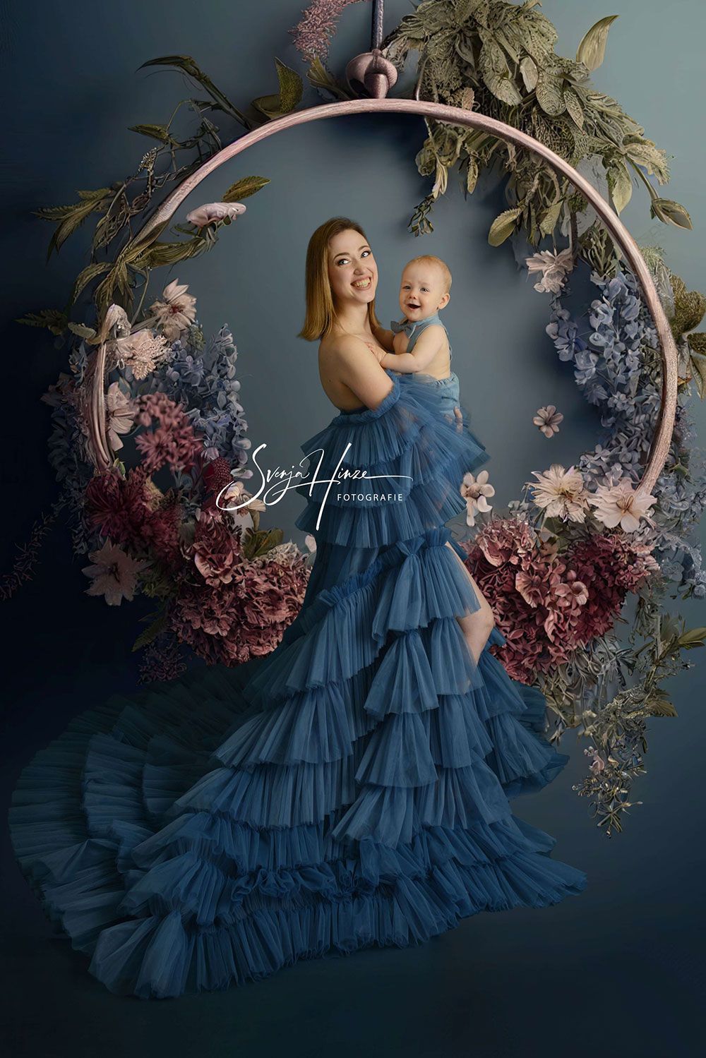 Eine Frau in einem blauen Kleid hält ein Baby in einem Blumenreifen.