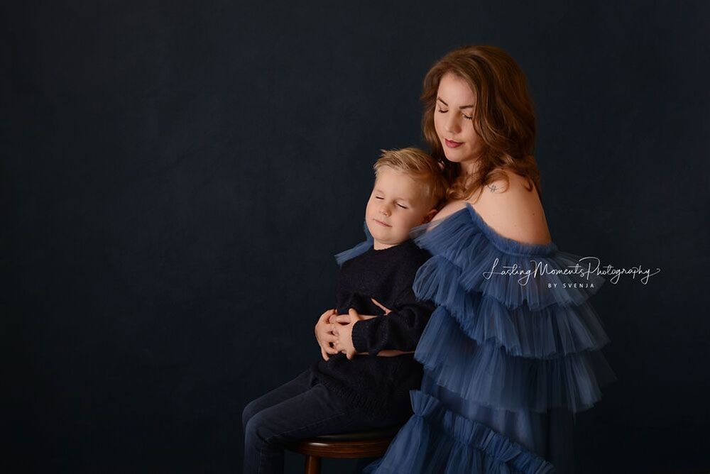 Eine Frau in einem blauen Kleid sitzt neben einem Jungen in einem schwarzen Hemd.