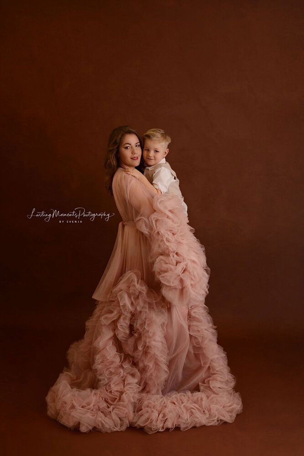 Eine Frau in einem langen rosa Kleid hält ein Kind.