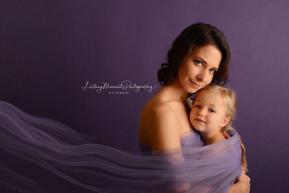 Eine Frau hält ein kleines Mädchen, das in ein lila Tuch gewickelt ist.