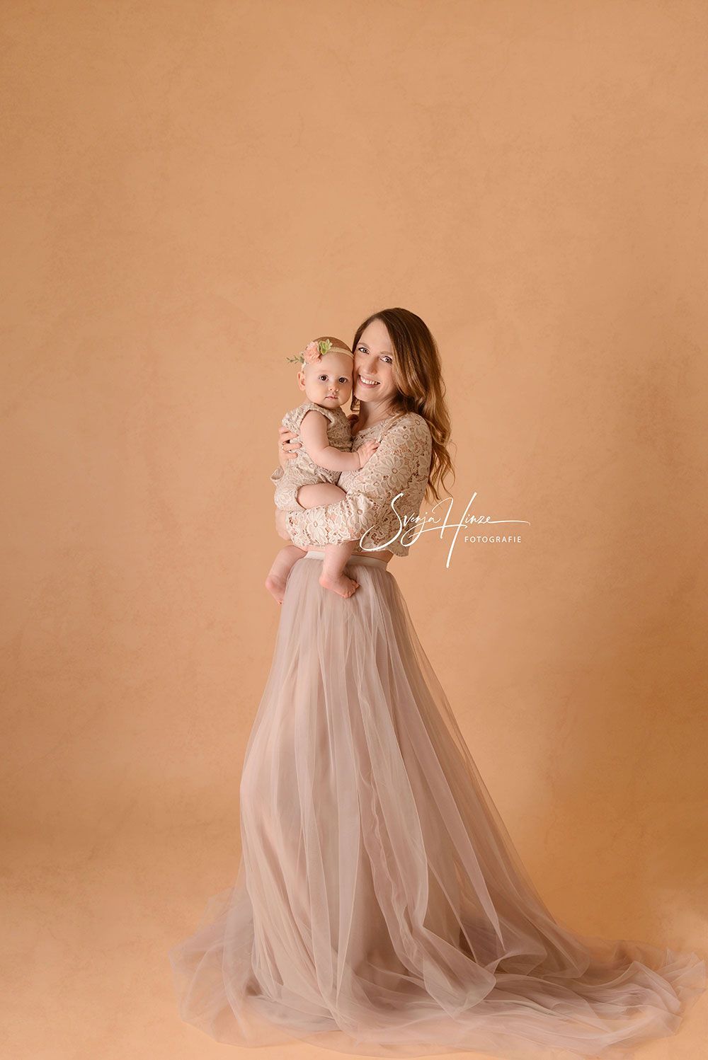 Eine Frau in einem langen Kleid hält ein Baby in ihren Armen.