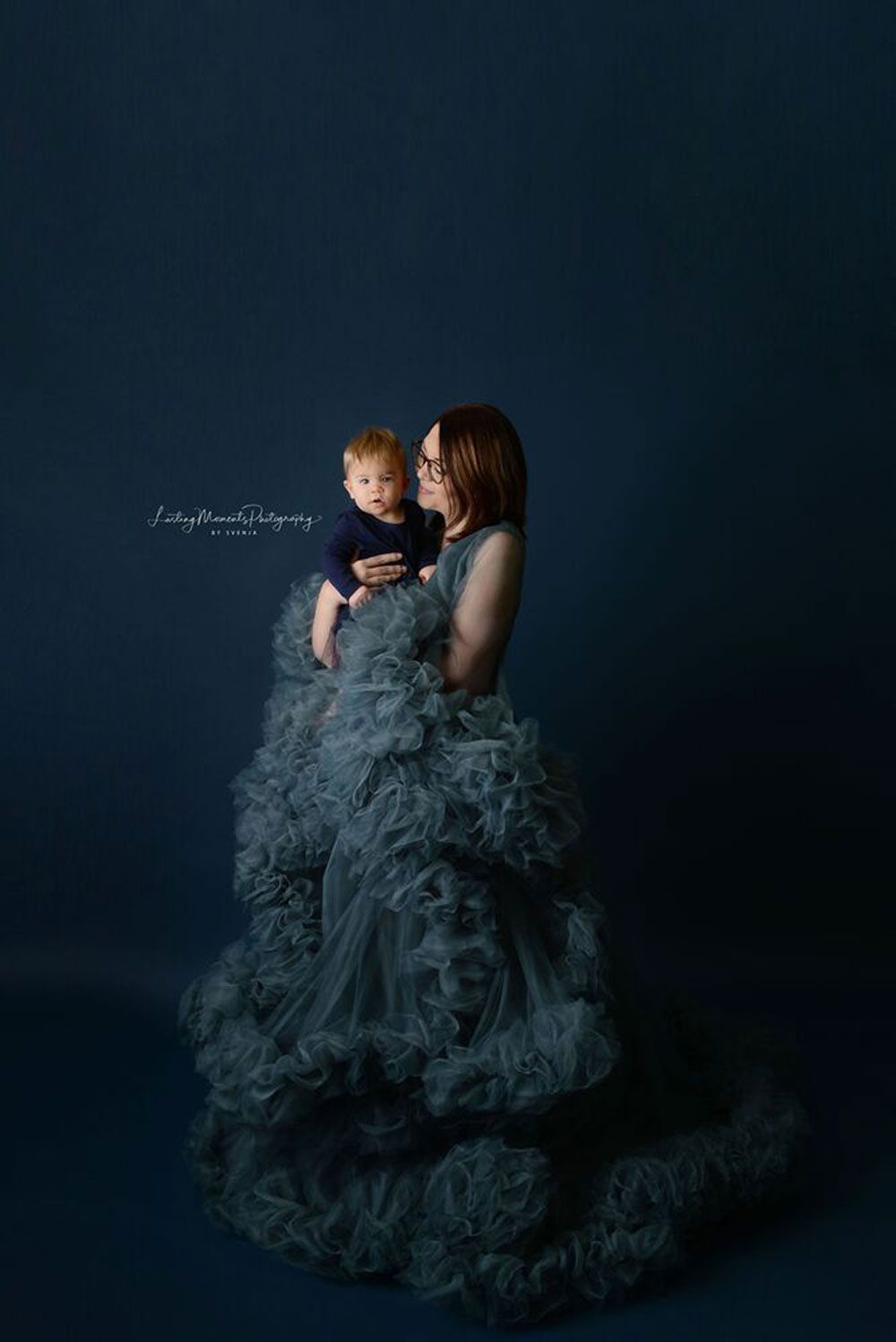 Eine Frau in einem langen Kleid hält ein Baby in ihren Armen.