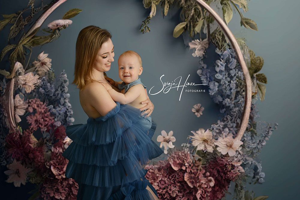 Eine Frau hält vor einem Blumenkranz ein Baby im Arm.