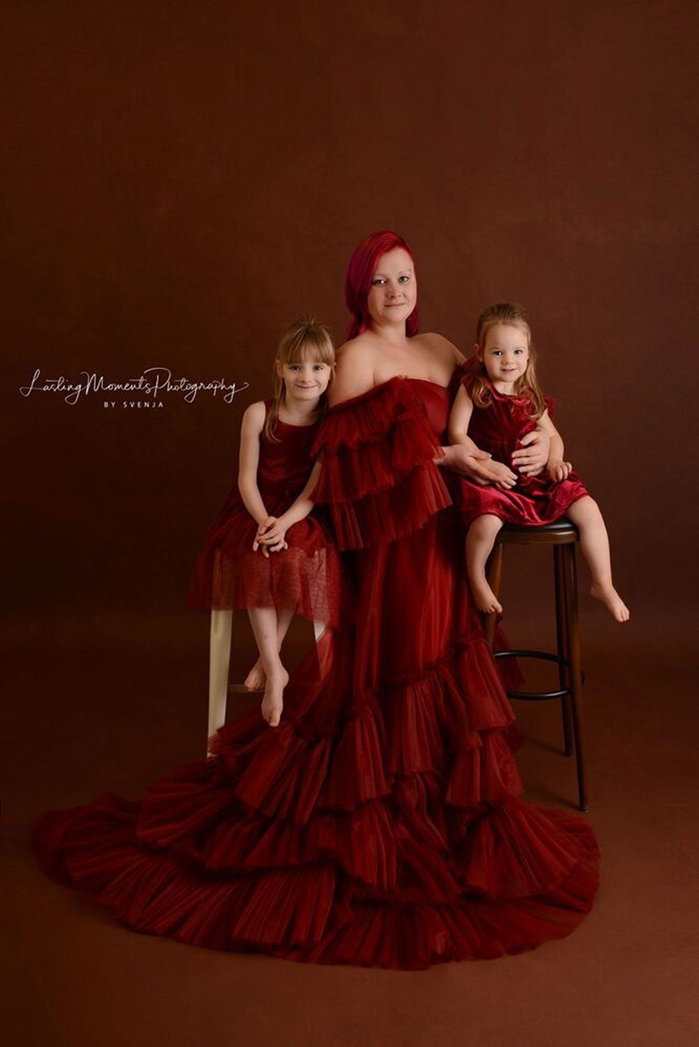 Eine Frau in einem roten Kleid posiert für ein Foto mit zwei kleinen Mädchen.