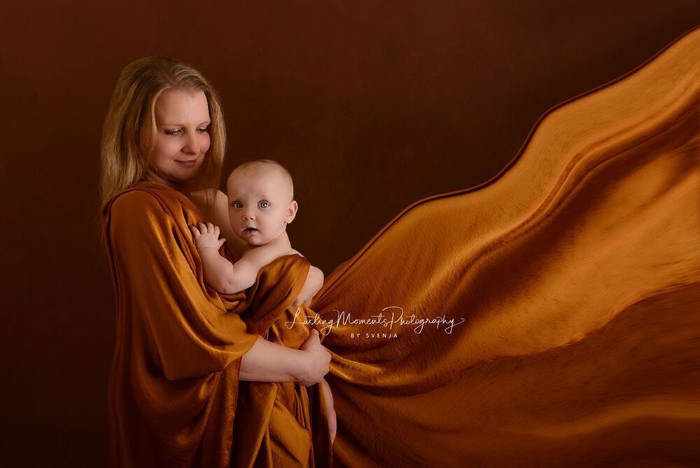 Eine Frau in einem langen orangefarbenen Kleid hält ein Baby.