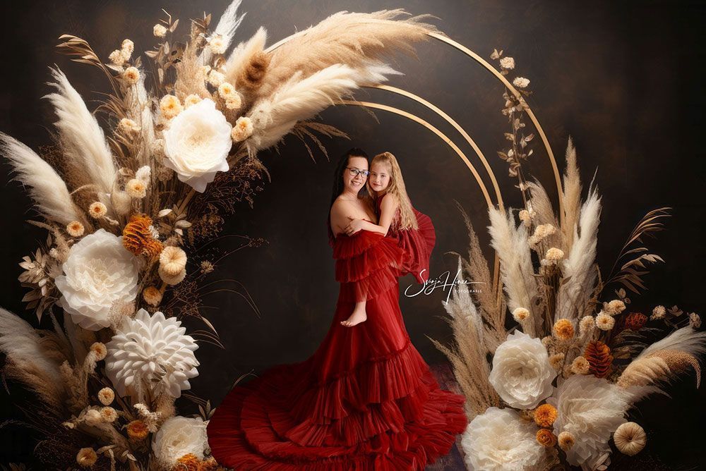 Eine Frau in einem roten Kleid hält ein Kind vor einem Blumenbogen.