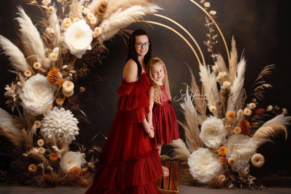 Eine Mutter und ihre Tochter posieren vor einer Blumenwand für ein Foto.