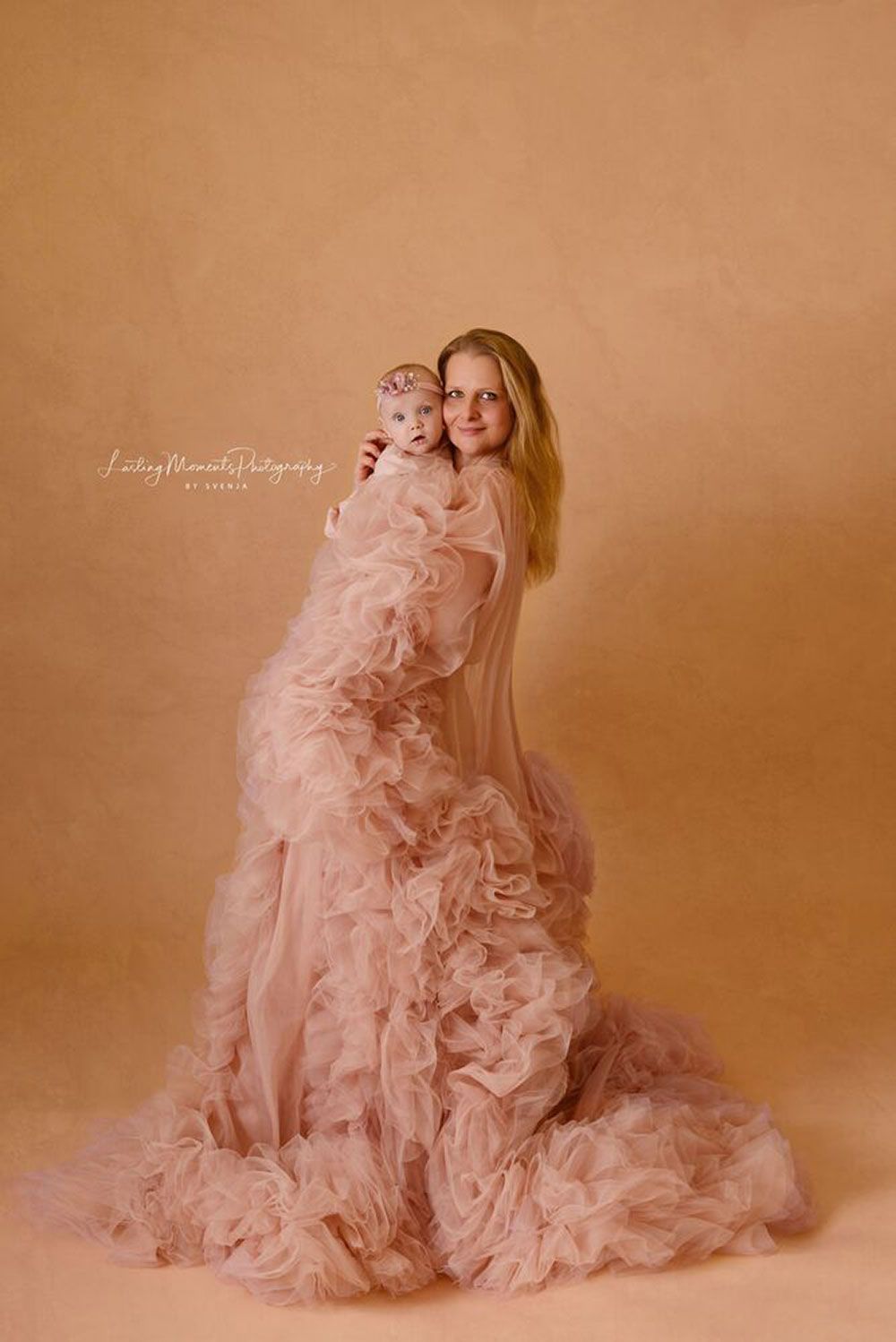 Eine Frau in einem langen rosa Kleid hält ein Baby.