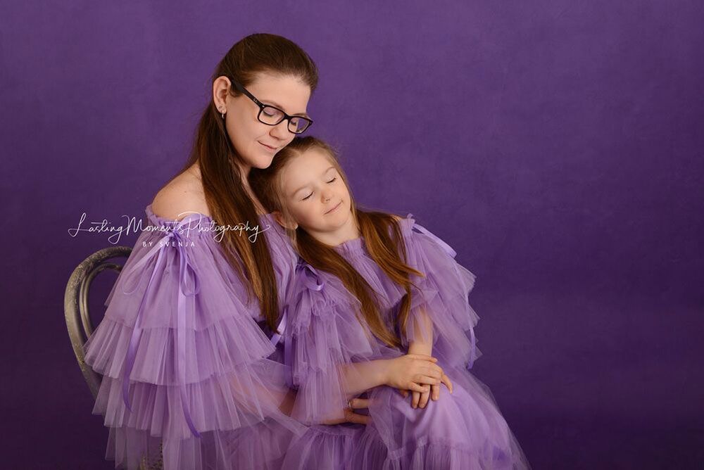 Eine Mutter und ihre Tochter sitzen in passenden lila Kleidern nebeneinander.