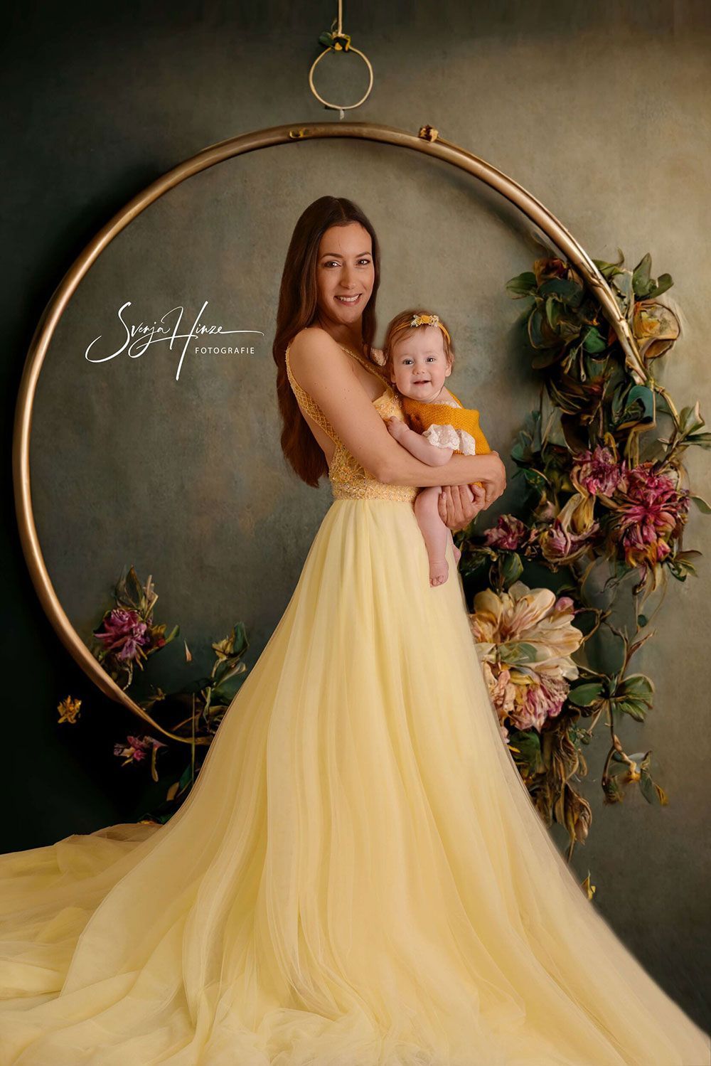 Eine Frau in einem langen gelben Kleid hält ein Baby in ihren Armen.