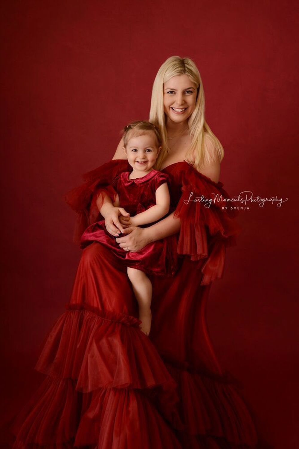 Eine Frau hält ein kleines Mädchen in einem roten Kleid.