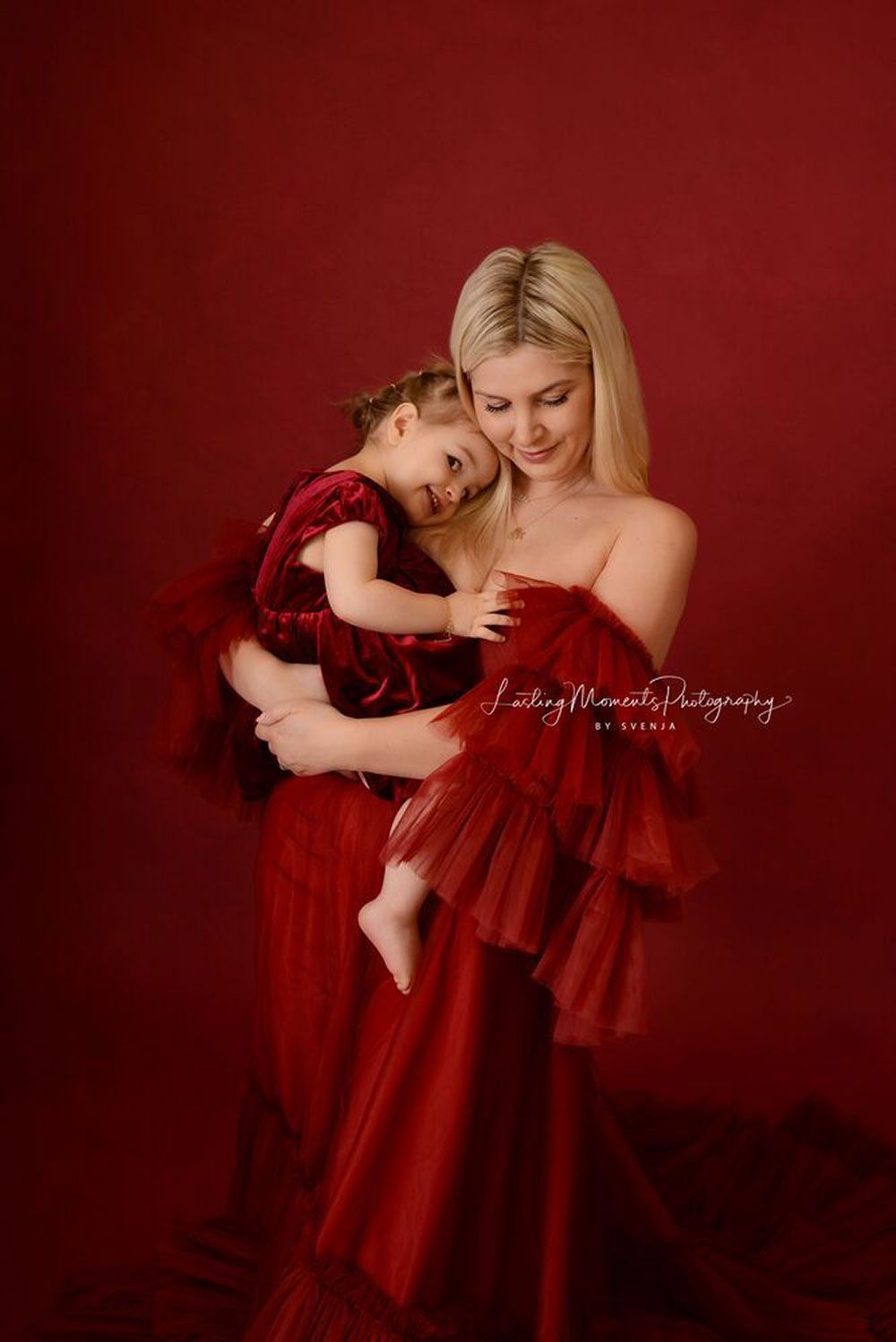 Eine Frau in einem roten Kleid hält ein kleines Mädchen in ihren Armen.