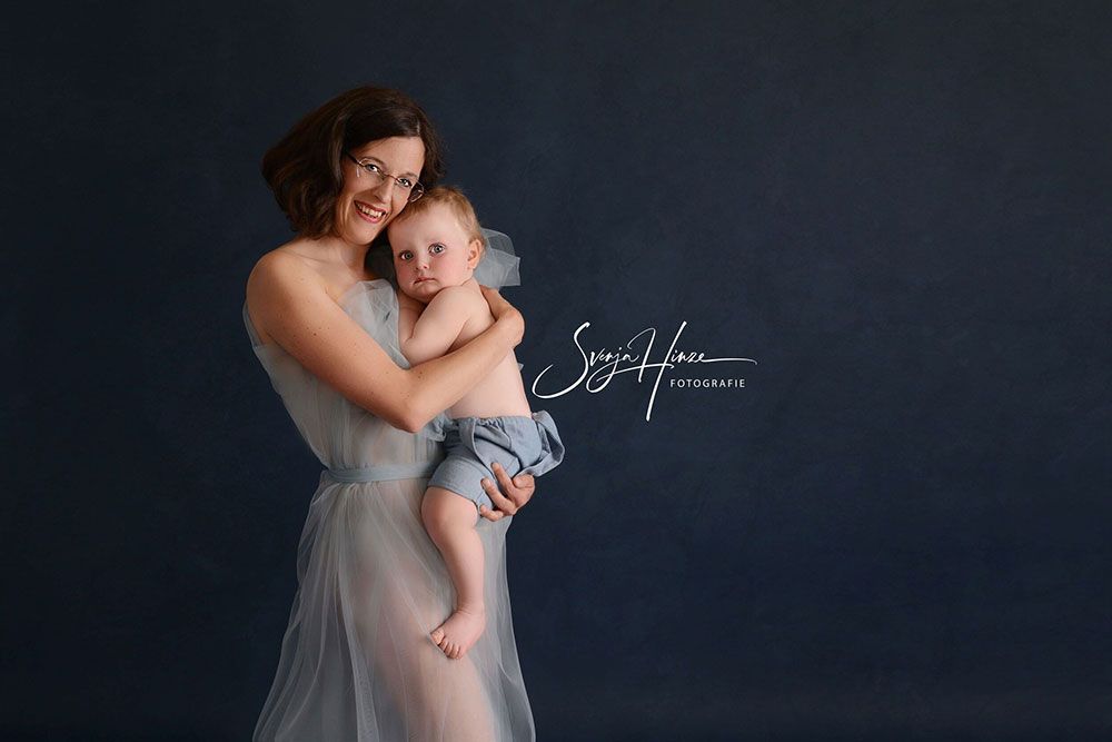 Eine Frau in einem blauen Kleid hält ein Baby in ihren Armen.