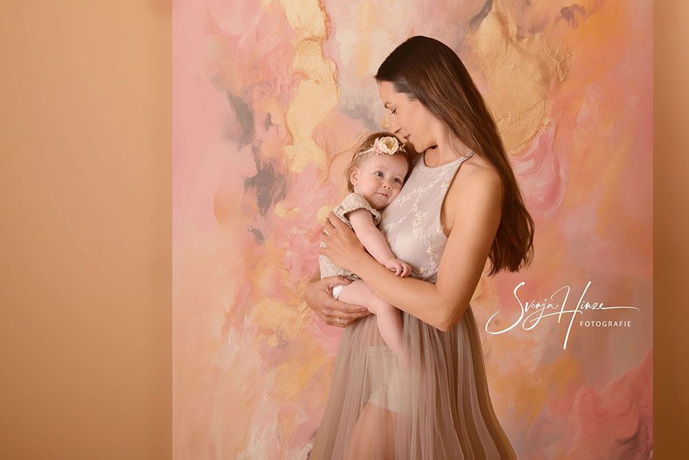 Eine Frau hält vor einem Gemälde ein Baby im Arm.