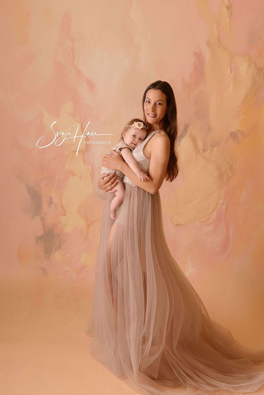 Eine Frau in einem langen Kleid hält ein Baby in ihren Armen.