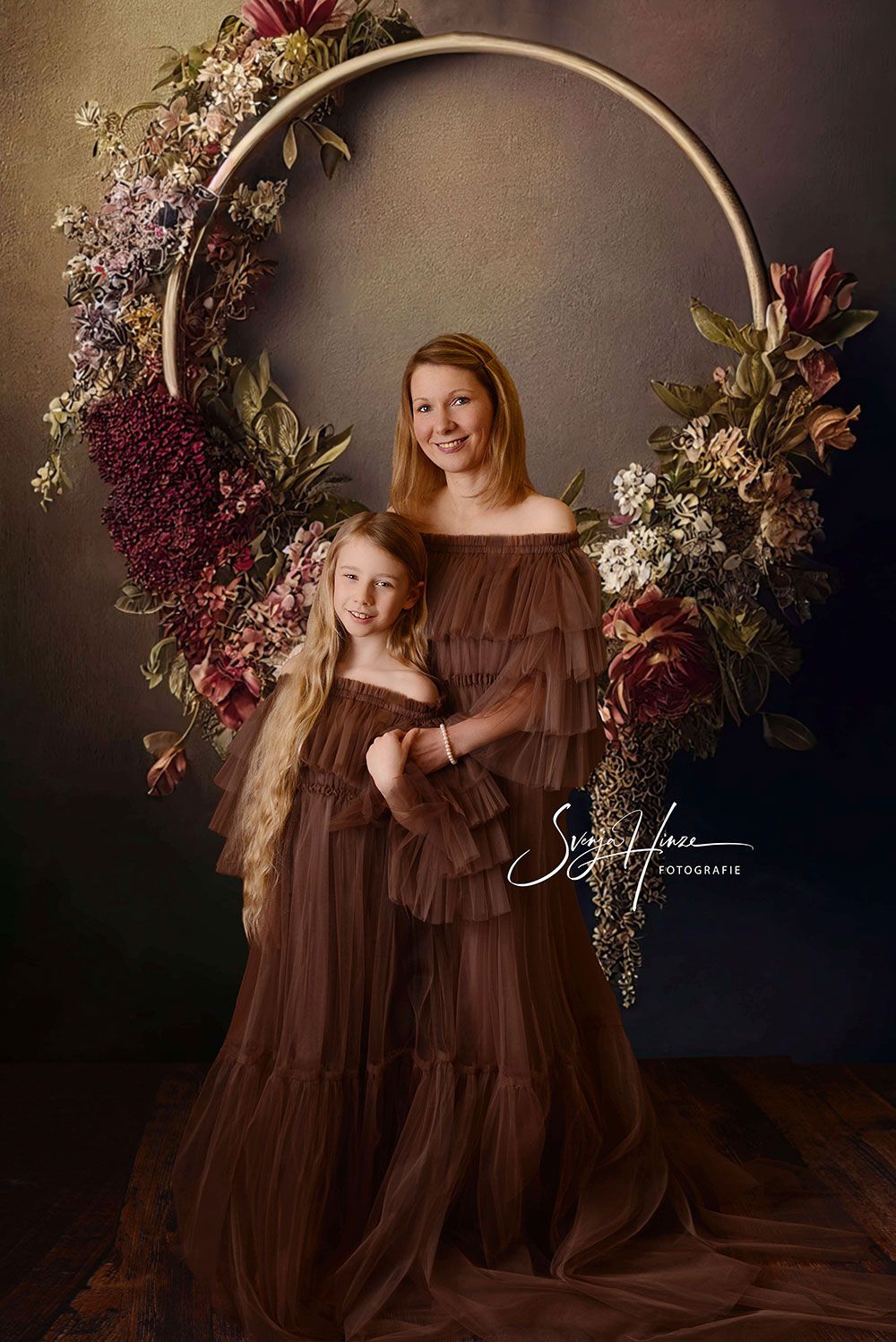 Eine Mutter und ihre Tochter posieren vor einem Blumenkranz für ein Foto.