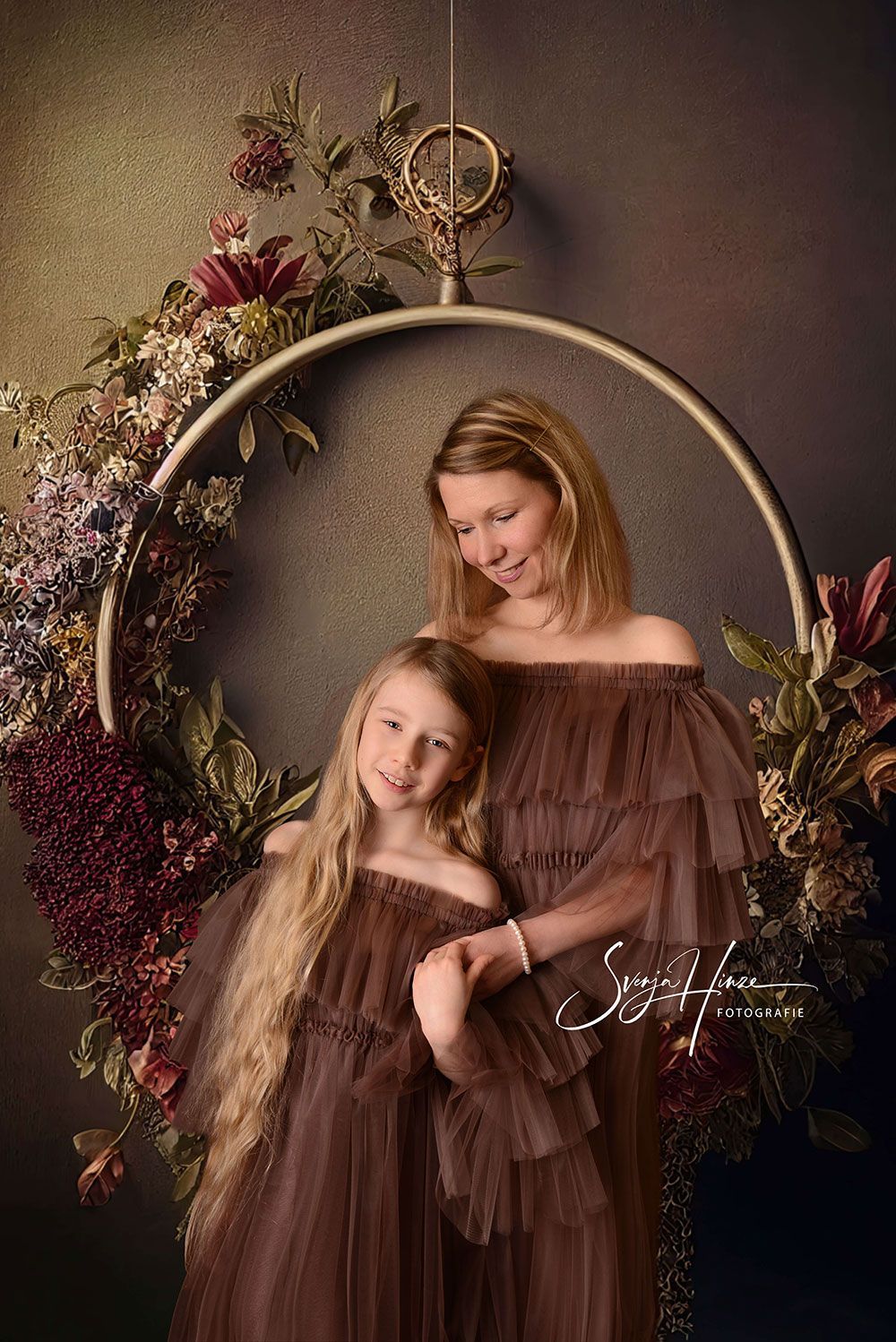 Eine Mutter und ihre Tochter posieren vor einem Blumenkranz für ein Foto.