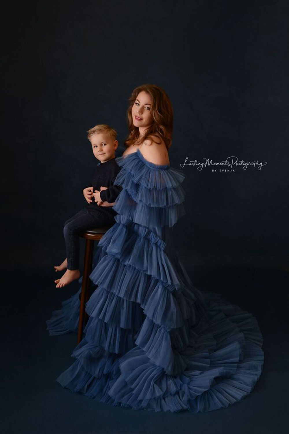 Eine Frau in einem blauen Rüschenkleid sitzt neben einem Jungen auf einem Hocker.