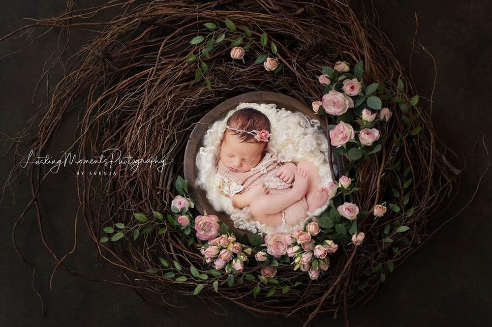 Ein neugeborenes Baby schläft in einem Nest, umgeben von Blumen.