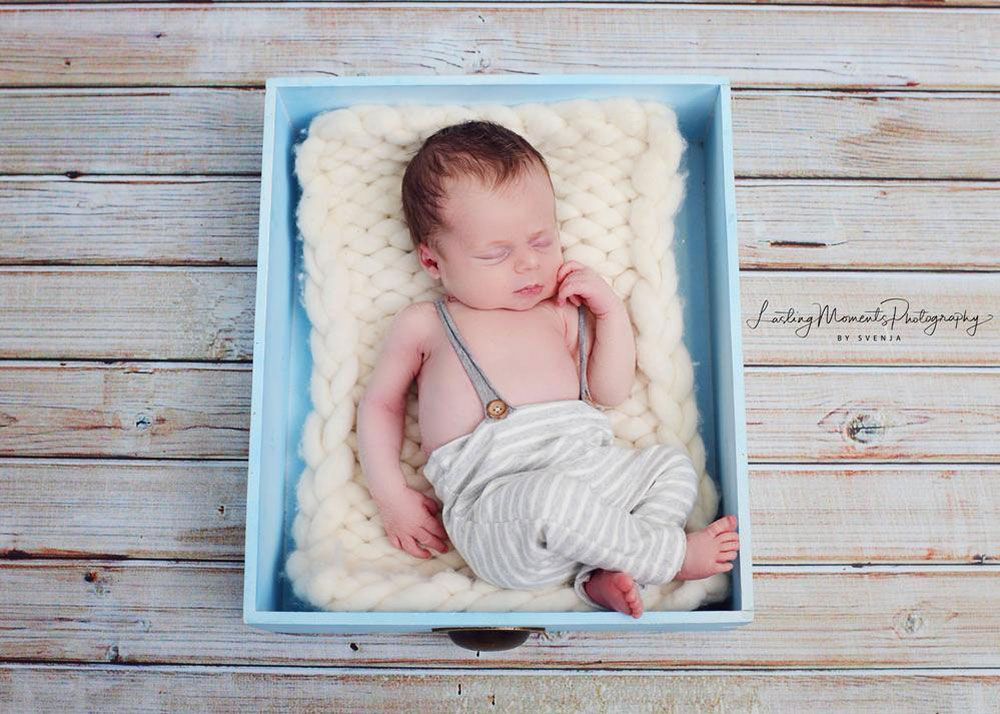 Ein Neugeborenes schläft in einer blauen Kiste auf einem Holztisch.