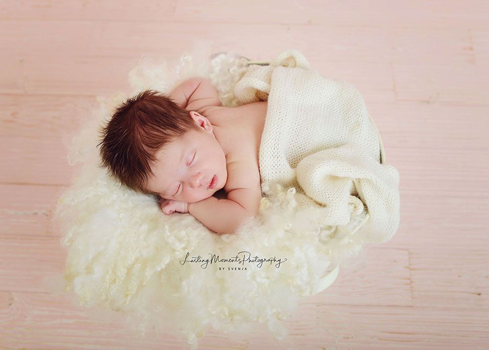 Ein Neugeborenes schläft auf einer weißen Decke auf einem Holzboden.