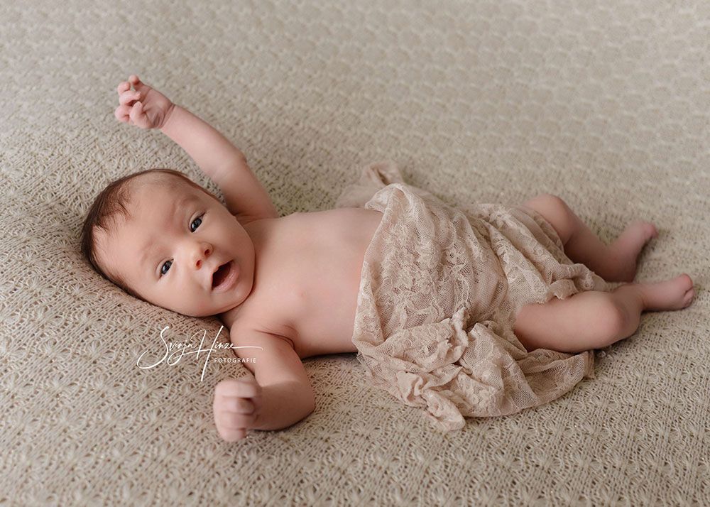 Ein in eine Decke gewickeltes Baby liegt auf dem Rücken auf einem Teppich.