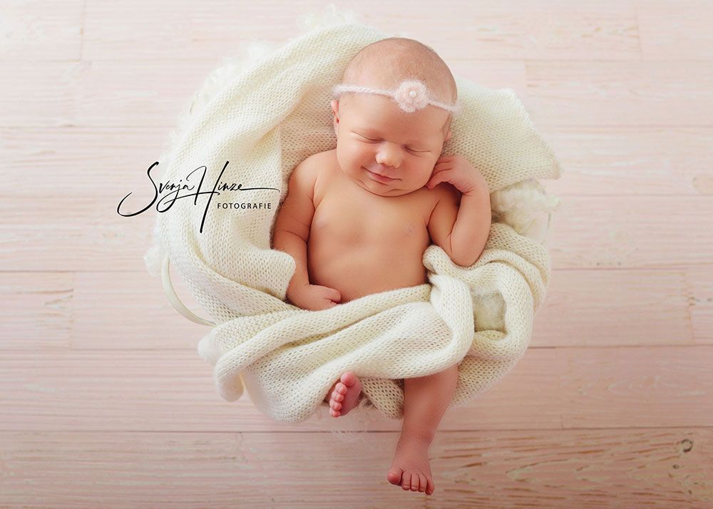 Ein Neugeborenes, in eine weiße Decke gewickelt, schläft auf einem Holzboden.