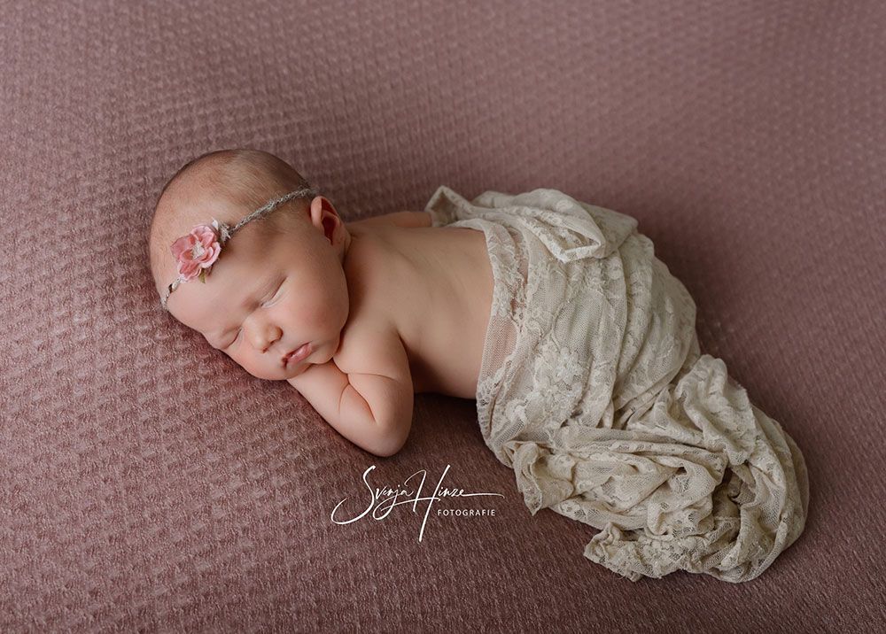 Ein in eine weiße Decke gewickeltes Neugeborenes schläft auf einer rosa Decke.