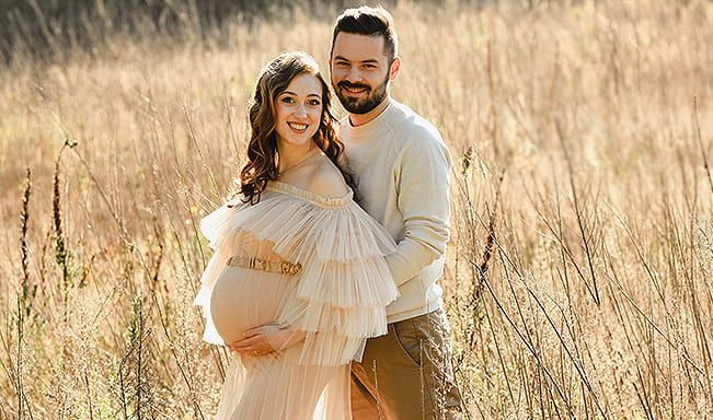 Ein Mann und eine schwangere Frau posieren auf einem Feld für ein Foto.