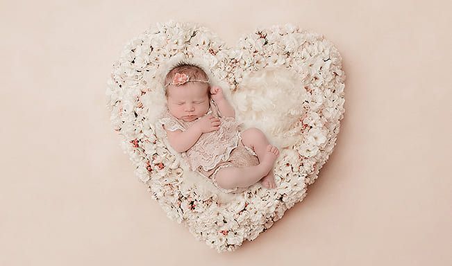 Ein Baby schläft in einem herzförmigen Korb aus Blumen.