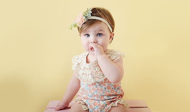 Ein kleines Mädchen sitzt mit der Hand im Mund auf einer Bank.