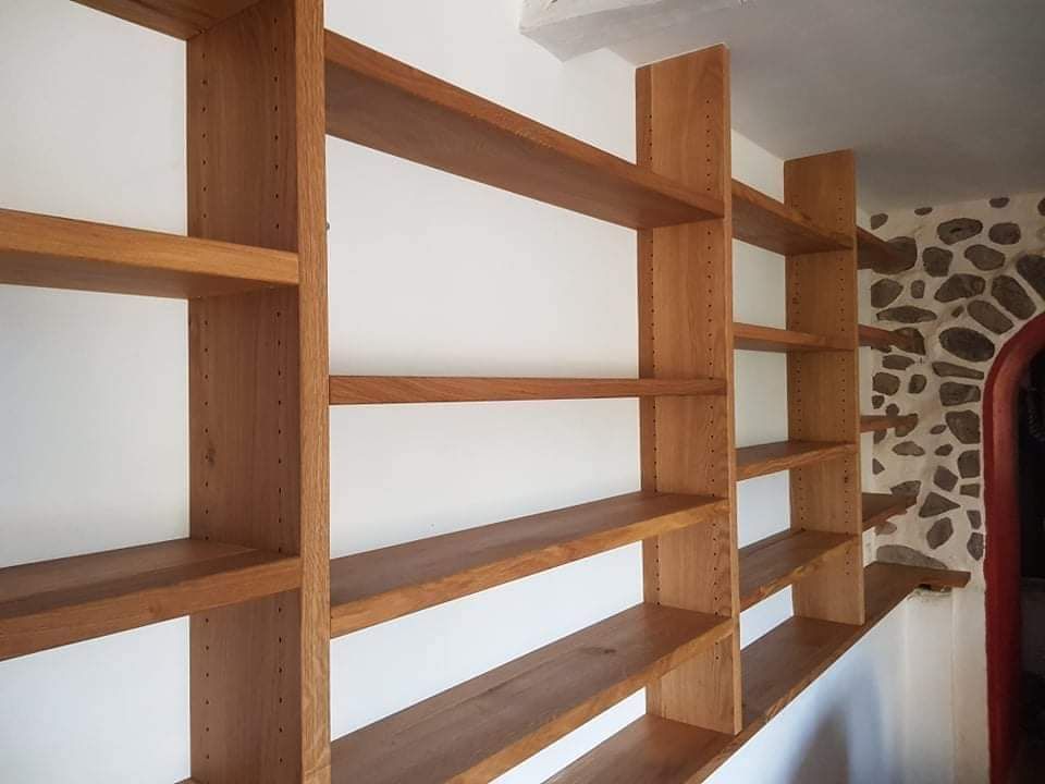 Étagères en bois encastrées contre un mur blanc et un mur en pierre avec une porte cintrée.