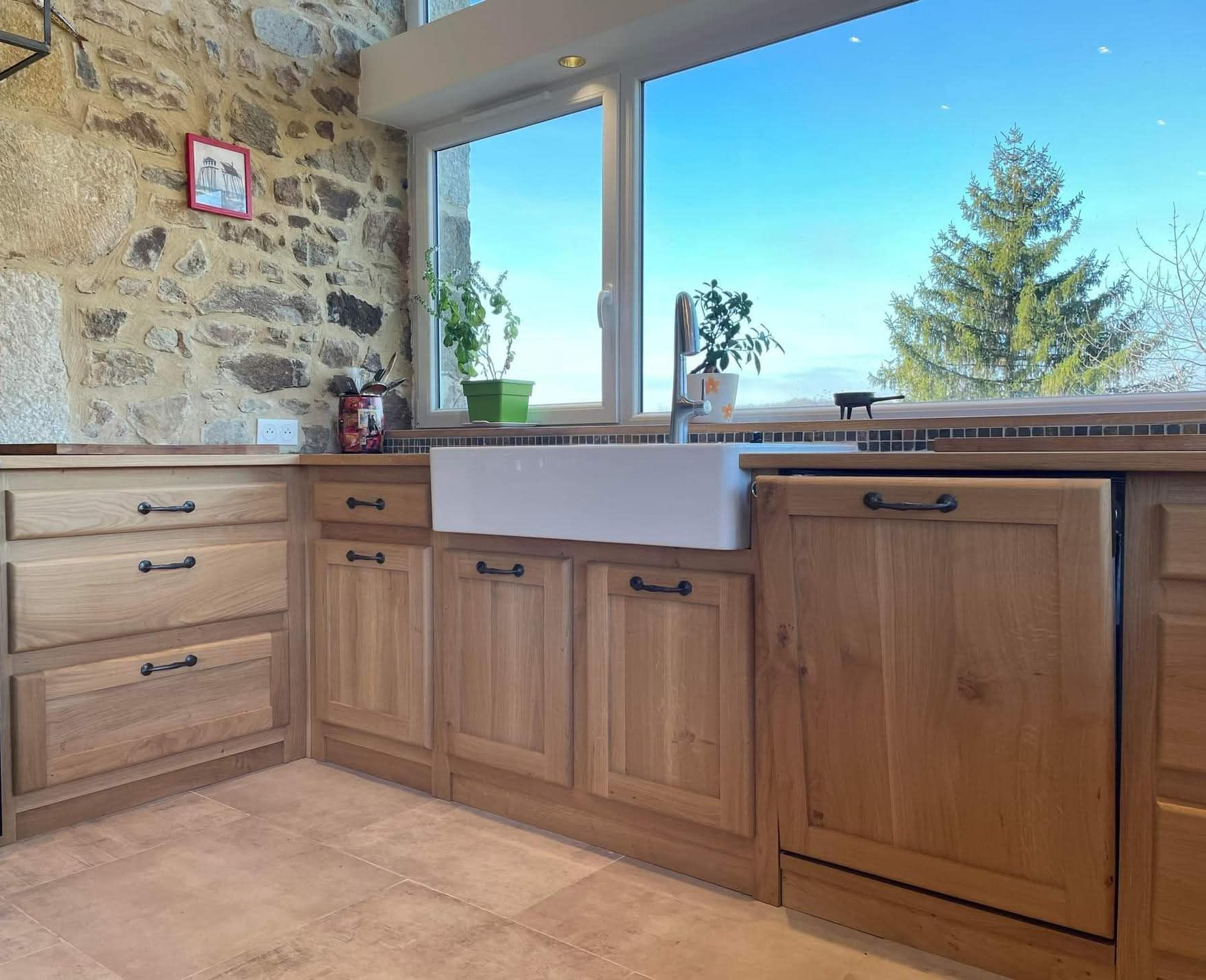 Cuisine en L avec armoires en bois clair, comptoirs foncés et appareils électroménagers en acier inoxydable.